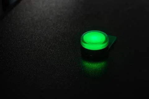 Small green illuminated button glowing on a textured black desk Stock Photos