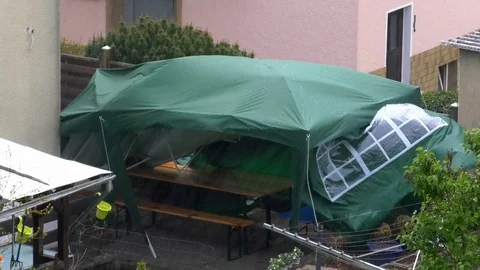 Small green party tent almost blown away by the wind on stormy rainy spring day Stock Footage 107086249