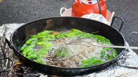 Small green peppers are cooked in oil in a large pot at a food fair. Pimientos Stock Footage 312340808