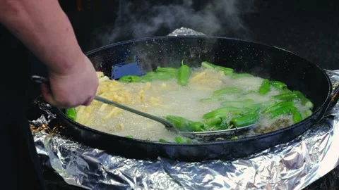Small green peppers are cooked in oil in a large pot at a food fair. Padron Stock Footage 317763966