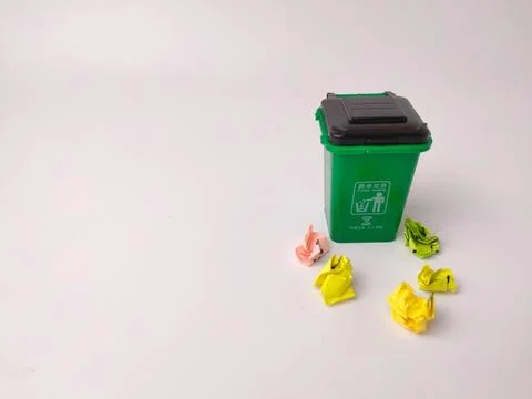 A small green plastic trash bin stands upright surrounded by crumpled bits .. Stock-Fotos