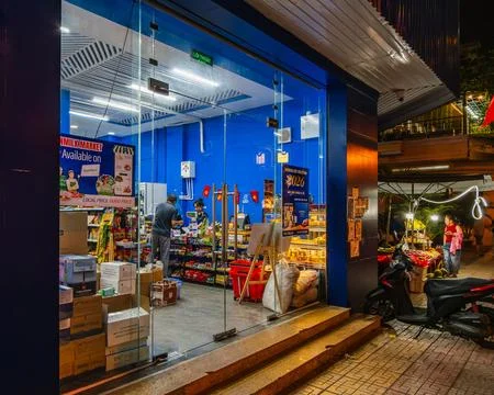 Small Grocery Store with Blue Interior and Glass Entrance at Night Stock-Fotos