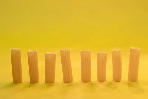 Small group of fresh macaroni rigati lined up on yellow background Stock Photos