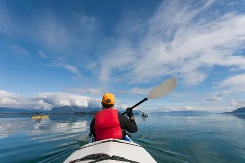 A small group of people kayaks in pristine waters of an inlet on the Alaska Stock Photos