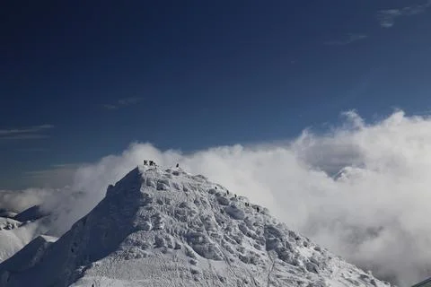 Small group at a snowy mountain summit above clouds Stock Photos