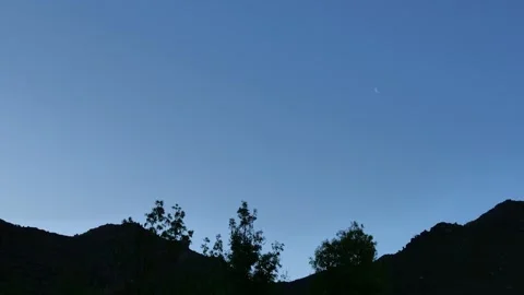 Small half moon on a pale blue sky with a mountain ridge in the foreground 4 Stock Footage 337557196