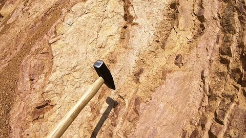 Small hammer hitting and cracking layer of limestone at some geology site Stock Footage 90247985