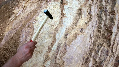 Small hammer hitting and cracking layer of limestone at some geology site Stock Footage 90261603