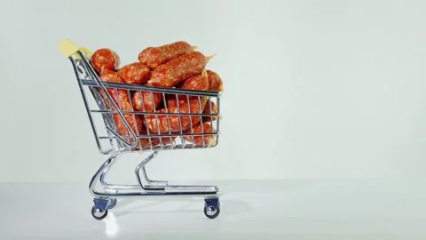 A small hand pushes tiny metal shopping cart filled with mini dry sausages .. Video stock 334519821