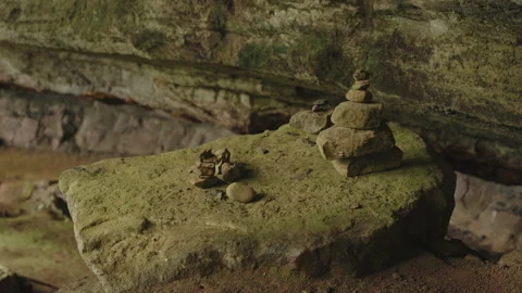 Small, hand-stacked stone cairns perched on a mossy boulder inside a rock 库存影片 336060425