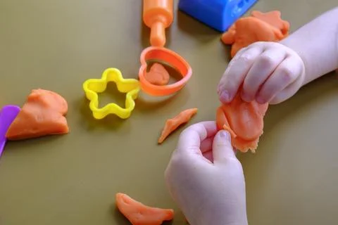 Small hands mold orange play dough with care 库存照片