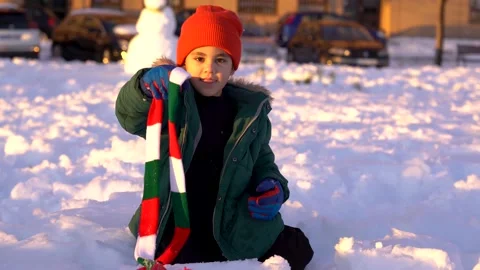 Small handsome boy removing scarf and smiling to camera in the snow sitting d Stock Footage 146474138