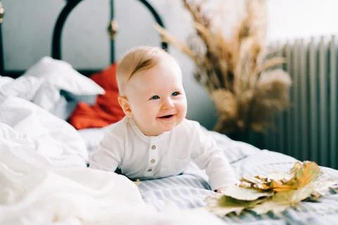 A small happy boy is lying on a light bed, smiling in a spacious Studio. fami Stock Photos