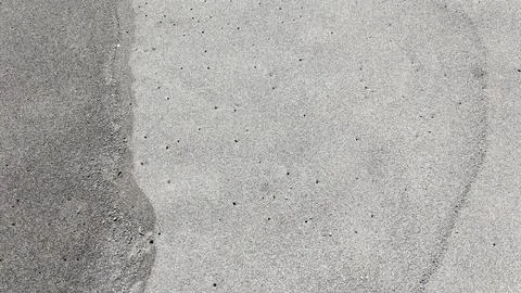 Small holes dot the surface of fine volcanic sand. A darker, damp patch of .. Stock Photos
