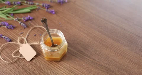 Small honey jar with spoon and blank craft tag on table. Fresh lavender stems Stock Footage 345422882