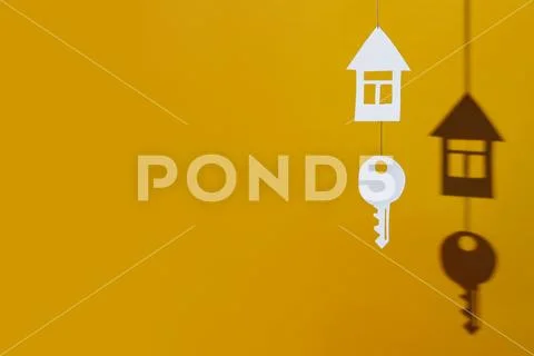 Small house and key made of cardboard casts a shadow on a bright colored back Stock Photos