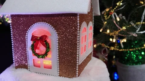 A small house with yellow lights in the windows rotates near Christmas trees Stock Footage 286298292