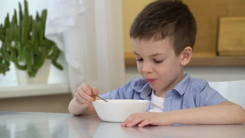 Small hungry boy eating tasting sweet corn flakes with milk at morning. Stock Footage 148323666