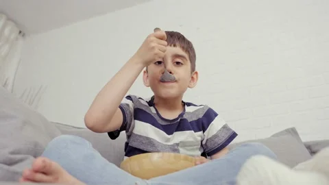 Small Hungry Boy Siting on Sofa, Eating Tasty Flakes With Milk Stock Footage 239067285