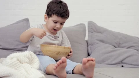 Small Hungry Kid Boy Eating Tasty Sweet Flakes With Milk For Breakfast Stock Footage 239066676