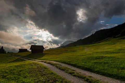 Small hut on mountain meadow with path and dramatic cloud sky Gerold Mittenwald Stock Photos