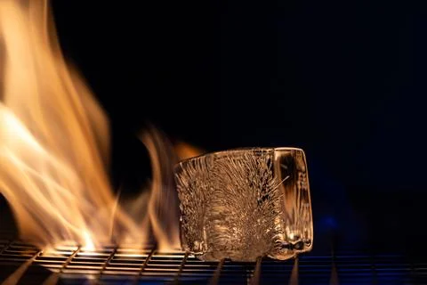 A small ice cube is sitting on a grill next to a flame Stock Photos