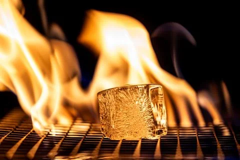 A small ice cube is sitting on a grill next to a flame Stock Photos