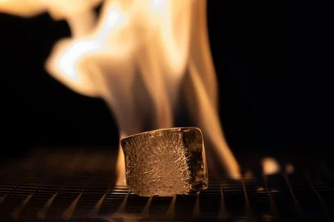 A small ice cube is sitting on a grill next to a flame Stock Photos