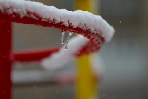 Small icicles hang on a metal bar covered with snow on a snowy winter day. Stock Photos