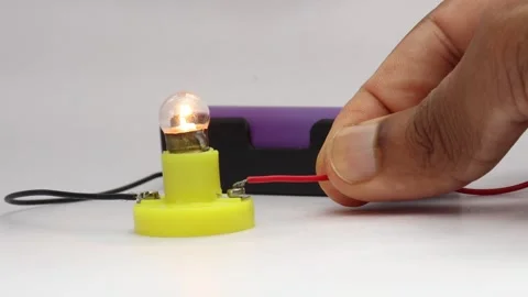 Small incandescent bulb glowing using power from a lithium polymer battery Stock Footage 341538920