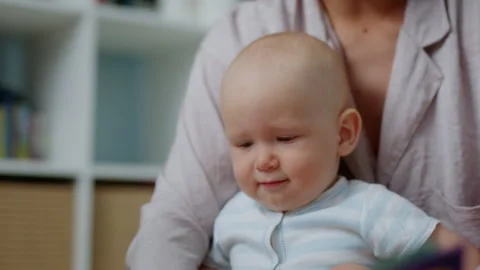 Small infant sits with his mother, looks at a book and listens to a fairy tale Stock Footage 303040082