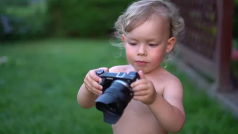 Small inquisitive three-year-old boy holds a professional camera with a lens in Video stock 155969326