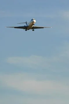 A small jet climbs through a bright blue sky with wisps of cloud below. Stock Photos