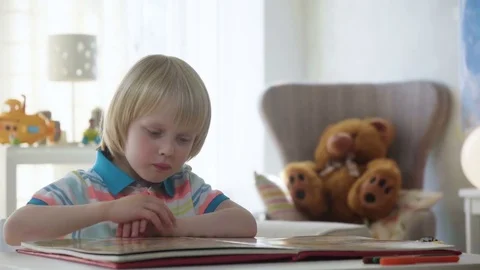Small kid boy opens and examines book with colorful illustrations with bright Stock Footage 78611016