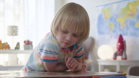 Small kid boy opens and examines book with colorful illustrations with bright Stock Footage 78611018