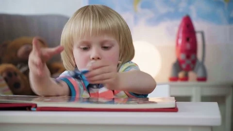 Small kid boy opens and examines book with colorful illustrations with bright Stock Footage 78611260