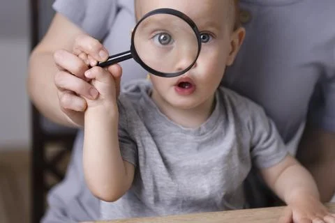 A small kid looks through a magnifying glass with a surprised look. Фото