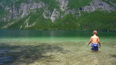 Small kid plays in shallow water of Bohinj lake, Slovenia Stock Footage 158016579