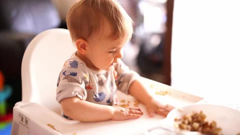 Small kid scatters nuts on the table, sitting on a high chair Stock-Footage 279731446