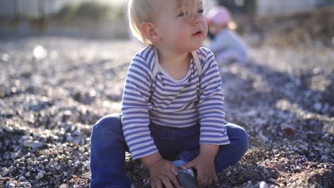 Small kid sits on the beach picks up small pebbles in his hands and pours them Stock Footage 256154826