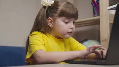 Small kid writes by pressing keyboard keys on computer. kid girl does her Stock Footage 220419089