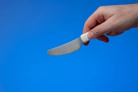 Small kitchen buttering spending knife with white plastic handle held by male Fotos de archivo