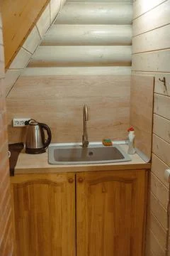 Small kitchenette featuring sink, kettle, and cleaning supplies in log cabin Stock-Fotos