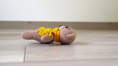 A small knitted cute toy bear (with yellow scarf) falls on the light floor 스톡 동영상 130490716