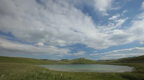 Small lake on a grassy glade with big cluds moving fast casting shadows Stock Footage 8603099