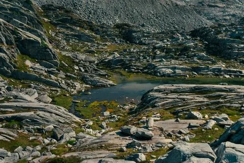 A small lake surrounded by rugged rocks and sparse vegetation in the hills. Stock Photos