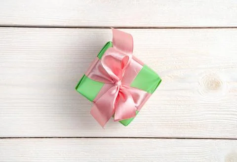 A small light green gift box with a pink ribbon on a white wooden background. Stock Photos
