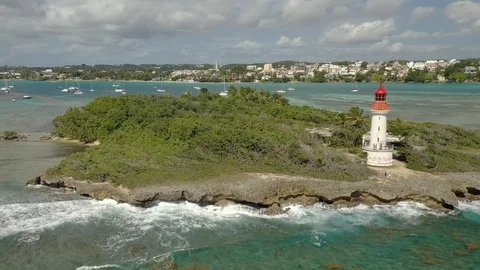 Small lighthouse island facing a busy resort shoreline in Guadeloupe 库存影片 101568719
