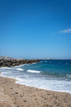 Small lighthouse on a rocky jetty by a beach on a sunny day. Stock Photos