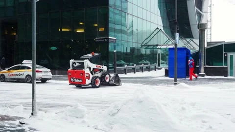 A small loader with a bucket removes snow from a road on a city street Stock Footage 149101698